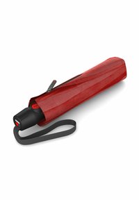Ombrello rosso dalla forma cilindrica lunga, con manico nero e chiusura con zip. Include una tracolla grigia per un facile trasporto.