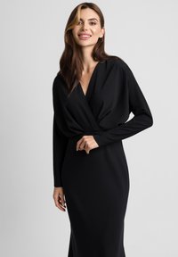 Czarna sukienka o kroju kopertowym z długimi rękawami, wykonana z gładkiego materiału; ma głęboki dekolt w kształcie litery V oraz dopasowany fason.