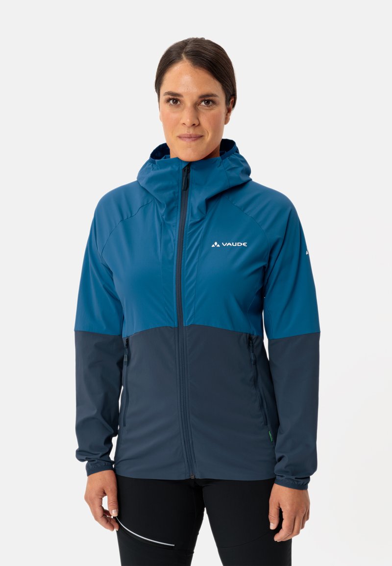 Veste coupe-vent bleu et marine avec capuche, fermeture éclair à l'avant, poches latérales et silhouette ajustée, fabriquée en tissu léger et lisse.