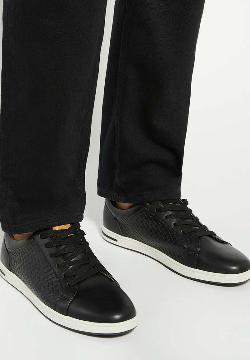 Black sneakers with textured synthetic and smooth leather upper, featuring a white rubber sole and black laces, designed for casual wear.