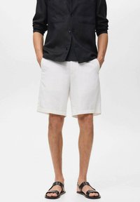Pantalones cortos de lino blancos con un corte relajado, que cuentan con bolsillos laterales. Combinados con una camisa de botones negra y sandalias negras.
