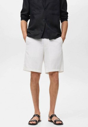 Pantalones cortos de lino blancos con un corte relajado, que cuentan con bolsillos laterales. Combinados con una camisa de botones negra y sandalias negras.