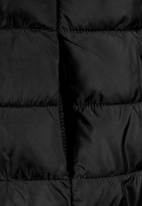 Veste matelassée noire en tissu quilté, avec des sections cousues, texture lisse, matériau léger et sans matériel visible.