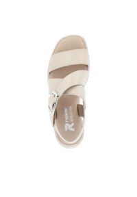 Sandale beige avec trois larges sangles et une boucle en argent décorative. Présente une semelle intérieure rembourrée et un design de bout arrondi pour le confort.