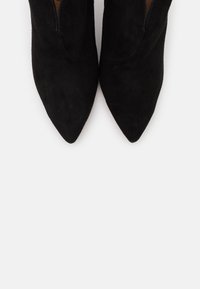 Botas de ante negras hasta el tobillo con un diseño de punta afilada. Presentan una textura suave y sin herrajes visibles. Los lados abiertos mejoran la transpirabilidad.