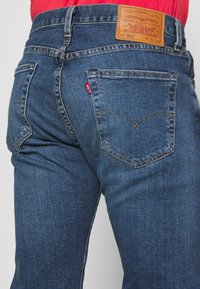 Blauwe spijkerbroek met een rechte pasvorm, leren label op de tailleband, en twee achterzakken met een kenmerkend gebogen stikselontwerp.