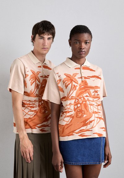 Polo à manches courtes, beige, avec une scène tropicale orange, incluant des palmiers et des personnages, fabriqué en tissu texturé, doté d'un col et de trois boutons.