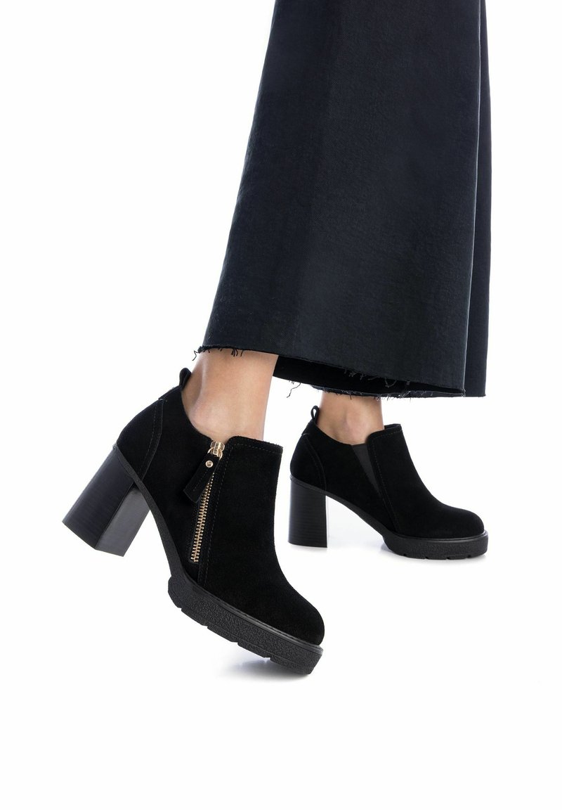 Botas de tobillo de ante negro con cierre de cremallera lateral, tacón grueso y suela de goma texturizada. Incluyen un diseño acolchado en el tobillo.