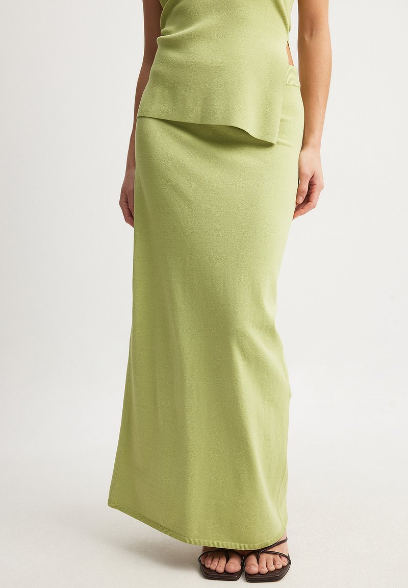 Grön stickad maxikjol med en slät textur, med en lagerdesign vid midjan och en figurnära silhuett. Accenterad med sandaler med remmar.