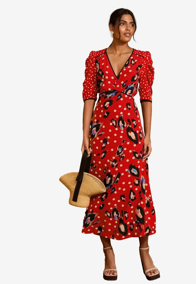 Rdeča obleka z globokim V-izrezom, naborki na rokavih ter vzorci pikic in leoparda. Tkanina je mehka; v kombinaciji s slamnato torbico in blok petami.