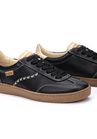 Baskets en cuir noir avec des lacets foncés, des accents crème et des surpiqûres contrastantes. Semelle en caoutchouc texturée avec un motif géométrique.
