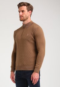 Brauner Reißverschluss-Pullover mit strukturiertem Rautenmuster, gerippten Bündchen und Saum. Hergestellt aus einem weichen Strickmaterial mit tailliertem Schnitt.