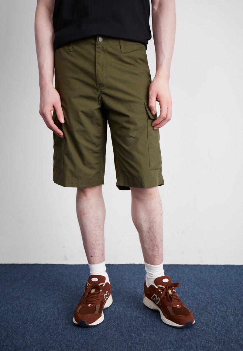 Olive green cargo shorts with a straight cut, front pockets, and a single side pocket, worn with brown sneakers and white ankle socks.