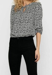 Blusa bianca e nera con piccolo motivo floreale, scollatura rotonda e dettaglio a occhiello, abbinata a jeans neri a vita alta.