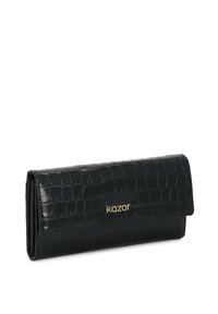 Melna gara maku uzglabāšanai ar spīdīgu krokodila tekstūru un zelta "kazar" logo uz priekšējā atloka, novietota uz baltas fona.