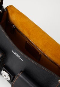 Sac à main en cuir noir avec un intérieur en suède orange, comportant une poche zippée et un logo en relief. Les accents cousus améliorent le design.