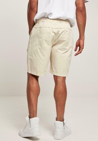 Beige shorts med en afslappet pasform, elastisk talje og to baglommer. Parrret med hvide høj-top sneakers. Ensfarvet tekstur.