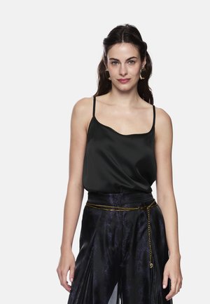 Black satin camisole with thin straps and a scalloped neckline, paired with dark, patterned wide-leg trousers and a gold chain belt.