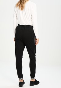 Pantalons de jogger noirs avec une taille élastique, des rayures blanches sur les côtés et des poignets côtelés. Texture de tissu lisse, coupe décontractée.