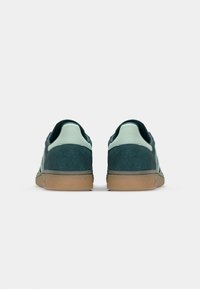 Vue arrière de baskets en daim teal avec un col en cuir vert clair et une semelle en caoutchouc gomme. Présente une tige texturée et des détails de couture subtils.