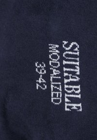 Marine gebreide stof met "DUURZAAM MODAL" en maatdetails in witte stiksels. Soepele textuur, met een strak ontwerp en minimale details.