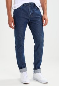 Slim-fit blå denimjeans med ljus tvätt, femficksdesign, uppvikta muddar och dragkedjeförslutning, matchade med vita sneakers.