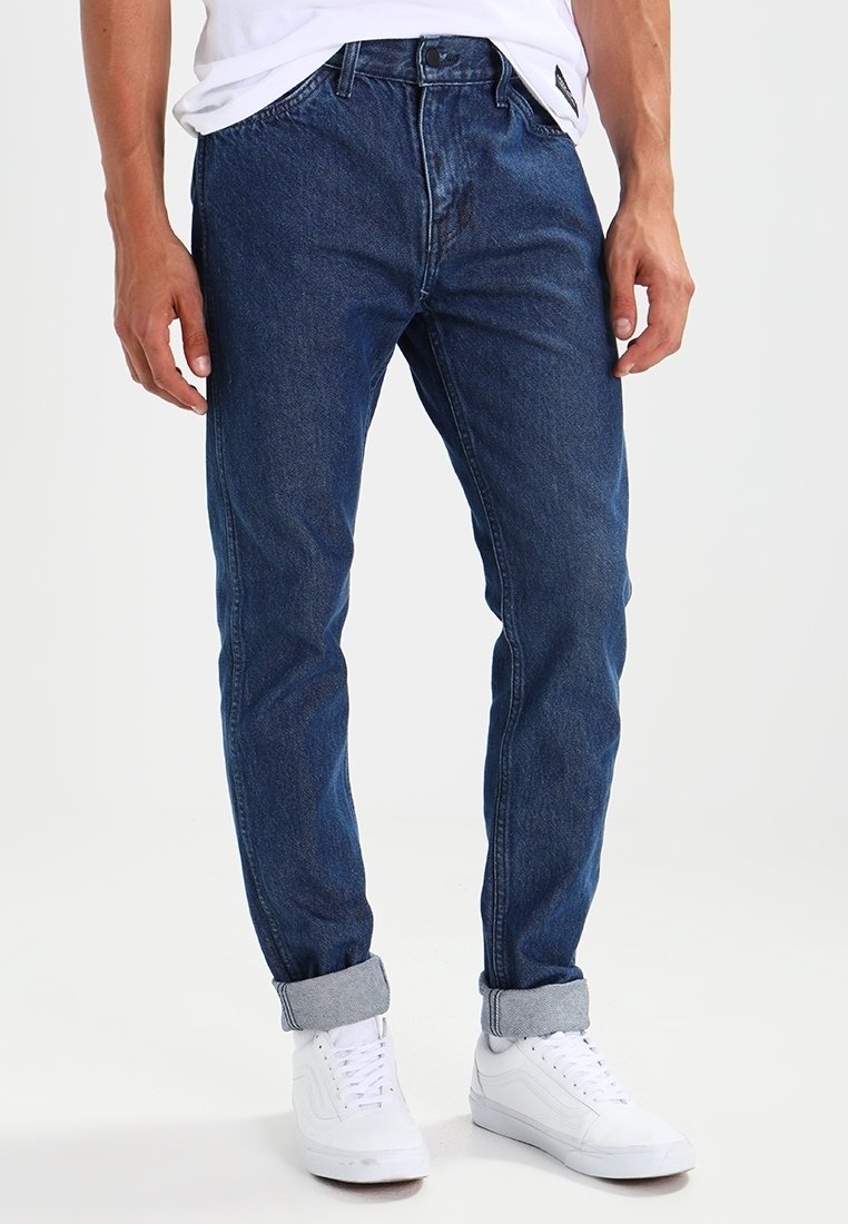 Slim-fit blå denimjeans med ljus tvätt, femficksdesign, uppvikta muddar och dragkedjeförslutning, matchade med vita sneakers.