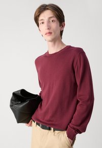 Maglione a maglia color bordeaux con maniche lunghe e scollatura tonda, abbinato a pantaloni khaki e con una borsa in pelle nera.