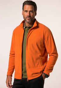 Orange fleece jacket with a zippered front and side pockets, layered over a green polo. The fabric appears soft and textured.