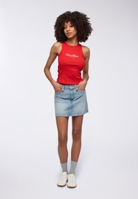 Top a cansone a coste rossa con il testo "Venice Beach" in bianco, abbinato a una gonna mini in denim azzurro chiaro, calze grigie e sneakers bianche.
