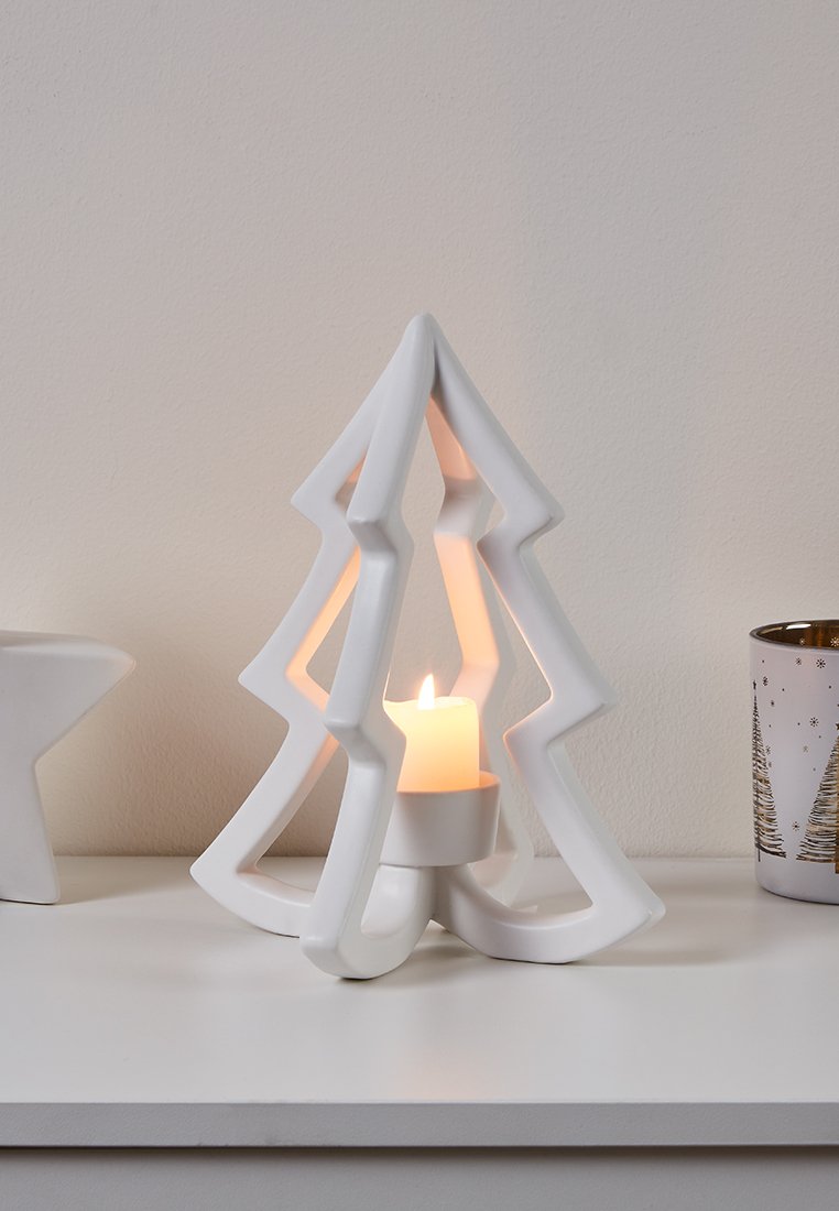 Weißer Kerzenhalter aus Keramik in Form eines Weihnachtsbaums, mit ausgestanzten Designs und einem zentralen Halter für eine Kerze, der sanftes Licht ausstrahlt.
