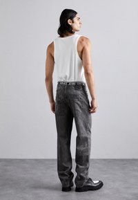 Jeans grii cu un finisaj texturat, brâu negru cu logo-ul "VERSACE JEANS COUTURE", asortați cu un tricou alb fără mâneci și pantofi negri.