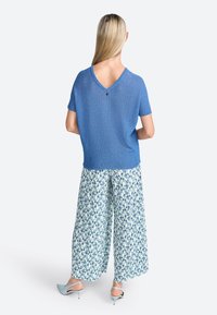 Top de punto azul de manga corta con escote en V y detalle de botones en la espalda, combinado con pantalones anchos impresos con flores en tonos verdes y azules, y tacones de color azul claro.