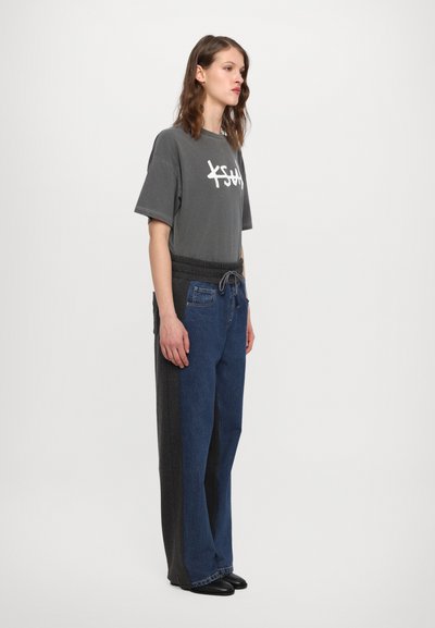 Camiseta gris con logo blanco, combinada con pantalones de pierna ancha que presentan un diseño dividido en gris oscuro y denim azul. Textura suave.