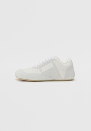 Zapatilla blanca hecha de cuero y ante con un acabado suave, que cuenta con un interior acolchado, cordones lisos y detalles de costura sutiles.