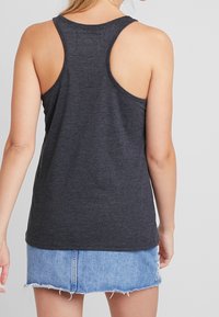 Top in grigio scuro senza maniche con design racerback. Realizzato in un tessuto leggero, presenta una superficie liscia e una vestibilità comoda. Abbinato a una gonna in denim.