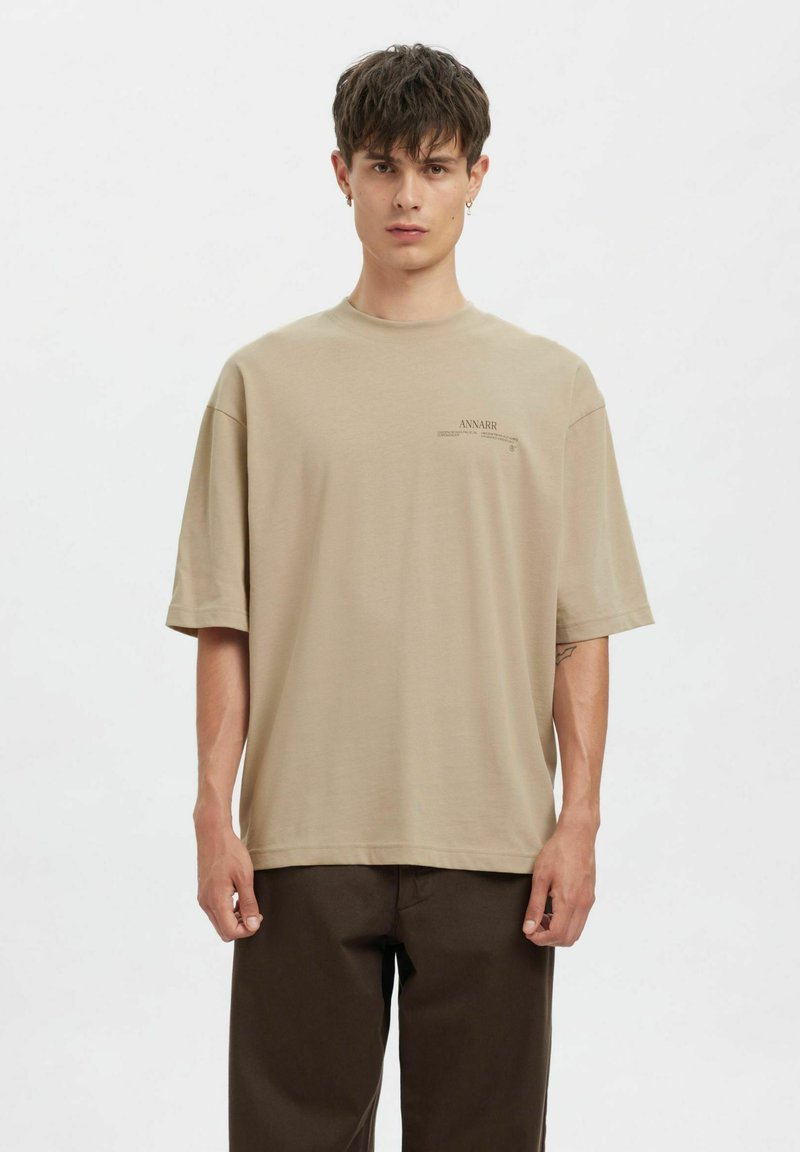 Béžové oversized tričko z měkké látky. Kulatý výstřih, krátké rukávy a malý potisk loga na levé straně. Rovný lem.