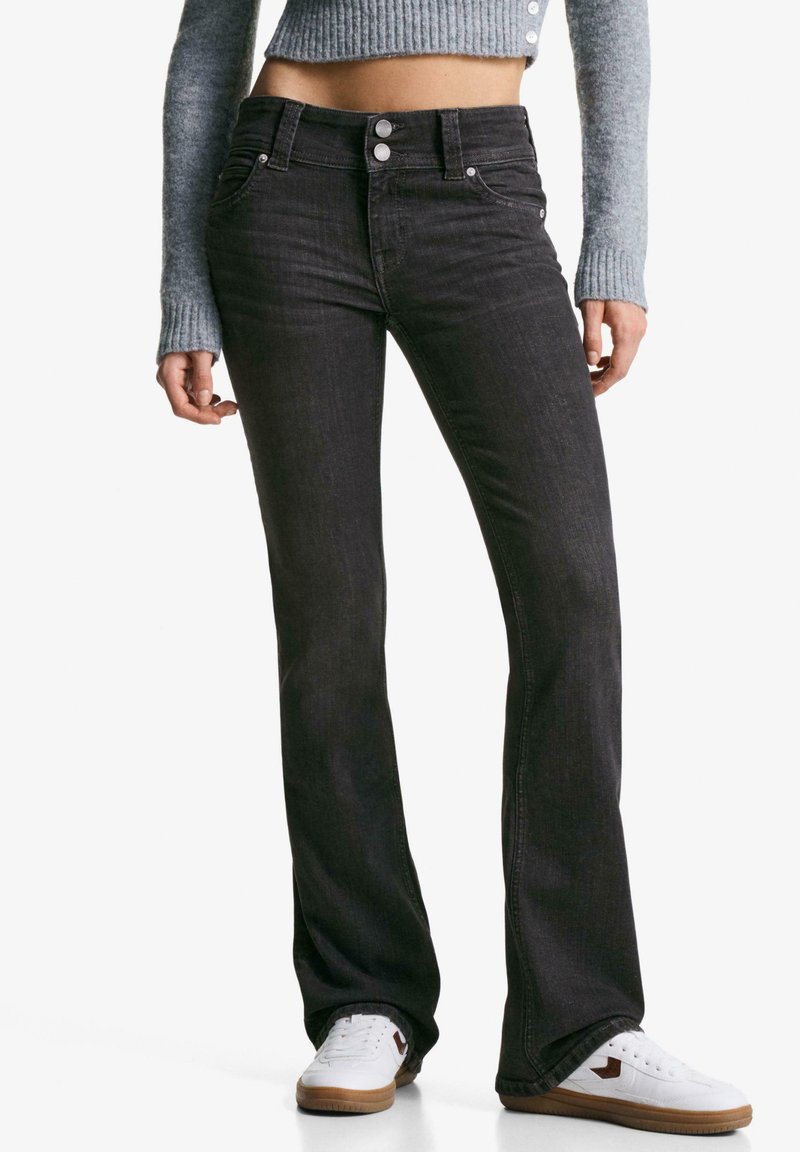 Black denim flared jeans with five pockets, metal buttons, and a mid-rise waist, paired with white sneakers and a gray cropped sweater.