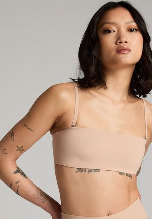 Top bandeau nude avec de fines bretelles réglables en tissu lisse et extensible. Présente un design minimaliste avec des bords lisses et sans couture.