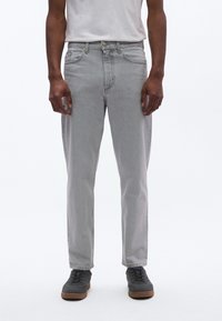 Svetlošedé rifle z denimu s priamym strihom, dizajnom s piatimi vreckami a jemnými švami. Nosené s bielym tričkom a tmavými teniskami.