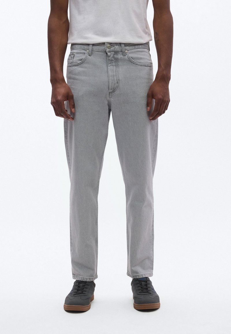 Svetlošedé rifle z denimu s priamym strihom, dizajnom s piatimi vreckami a jemnými švami. Nosené s bielym tričkom a tmavými teniskami.