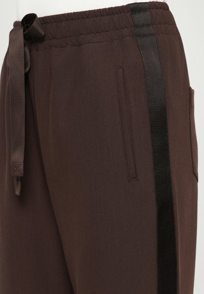 Pantalons marron avec taille élastique, cordon de serrage, poches latérales et une bande verticale noire le long de la jambe extérieure.