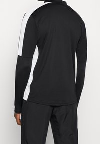 Long-sleeve athletic shirt in black with white side panels. Made of lightweight, smooth fabric. Features a high collar and fitted design.