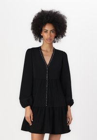 Robe noire avec un décolleté en V, de longues manches bouffantes et une jupe plissée. Présente des rivets en argent décoratifs le long de la ligne de boutons. Texture lisse.