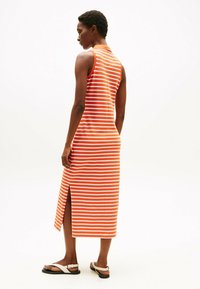 Sukienka w paski w kolorach pomarańczowym i białym, bez rękawów, do kolan z bocznym rozcięciem, uzupełniona prostymi sandałami.