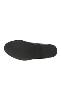 Sola nera di una scarpa con una superficie liscia, forma arrotondata e piccoli pattern di trazione lungo i bordi. Nessun dettaglio di branding visibile.