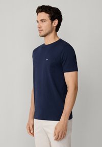 Granatowa, krótko rękawowa koszulka wykonana z bawełny. Posiada kieszonkę na piersi i okrągły dekolt. Gładka faktura i prosty design.