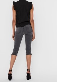 Pull noir avec une finition en dentelle aux épaules, associé à un jean cropped gris foncé. Des sandales à talons noires complètent la tenue.