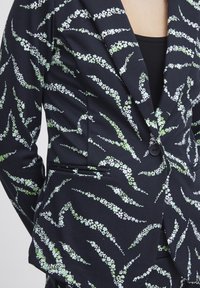 Czarna marynarka z białym i zielonym wzorem w kwiaty, z pojedynczym zapięciem na guzik, slim fit, z klapami i kieszeniami po bokach. Teksturowana tkanina.