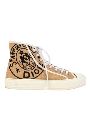 Baskets montantes en toile beige avec des lacets blancs, une semelle en caoutchouc et un logo circulaire noir avec un motif de texte sur le côté.